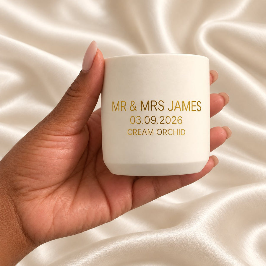 Personalised 90g wedding candle held in a neatly manicured hand on ivory satin