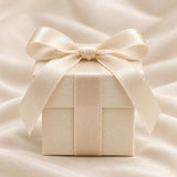 A square, cream-coloured gift box with a textured surface, wrapped in a matching satin ribbon tied into a bow on top. The box features a clean, structured design with a lid that sits flush against the base, centred with a smooth ribbon.