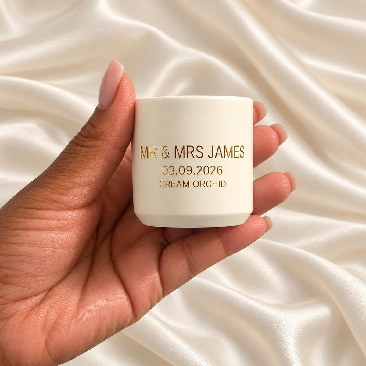 Personalised 40g Candle Wedding Favours held in a neatly manicured hand on ivory satin