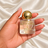 Maid of Honour gold ball cap perfume held in a neatly manicured hand on ivory satin