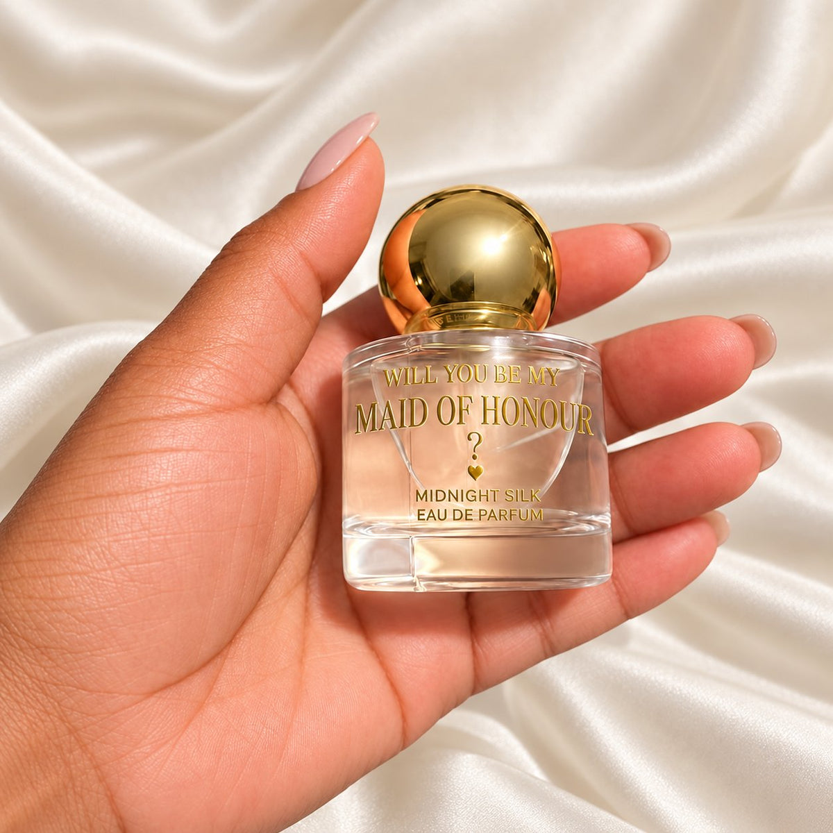 Maid of Honour gold ball cap perfume held in a neatly manicured hand on ivory satin