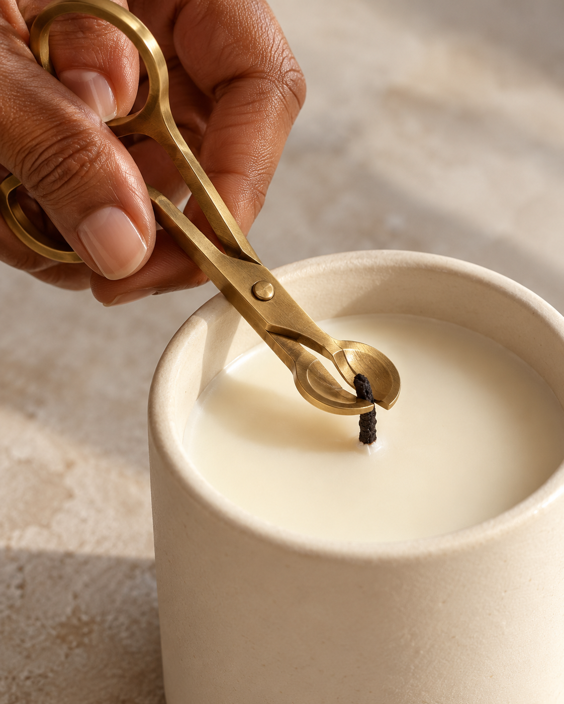 A hand trimming the wick of an unlit candle